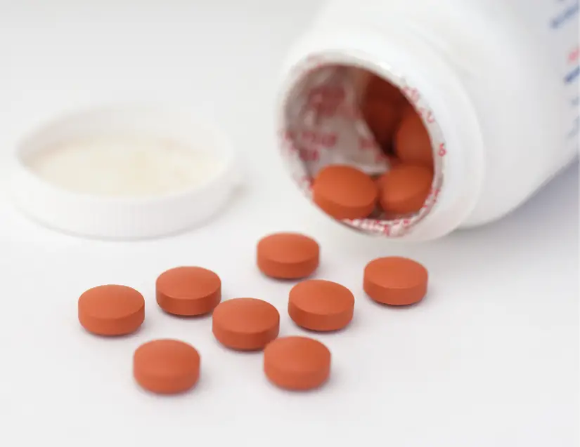 Do NSAIDs cause chronic back pain? Red circular pills spill out of bottle.